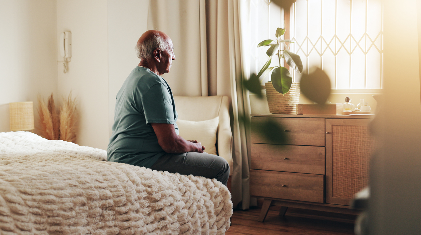 Senior man sitting alone on a bed considering SSI income rules for living arrangements.