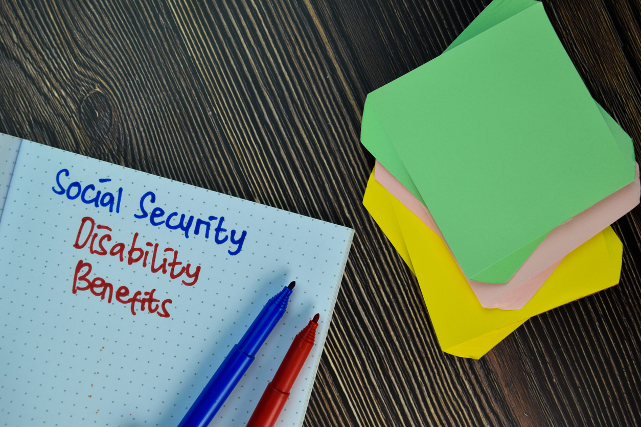 The words Social Security Disability Benefits written in a work notebook in blue and red ink beside a stack of sticky notes
