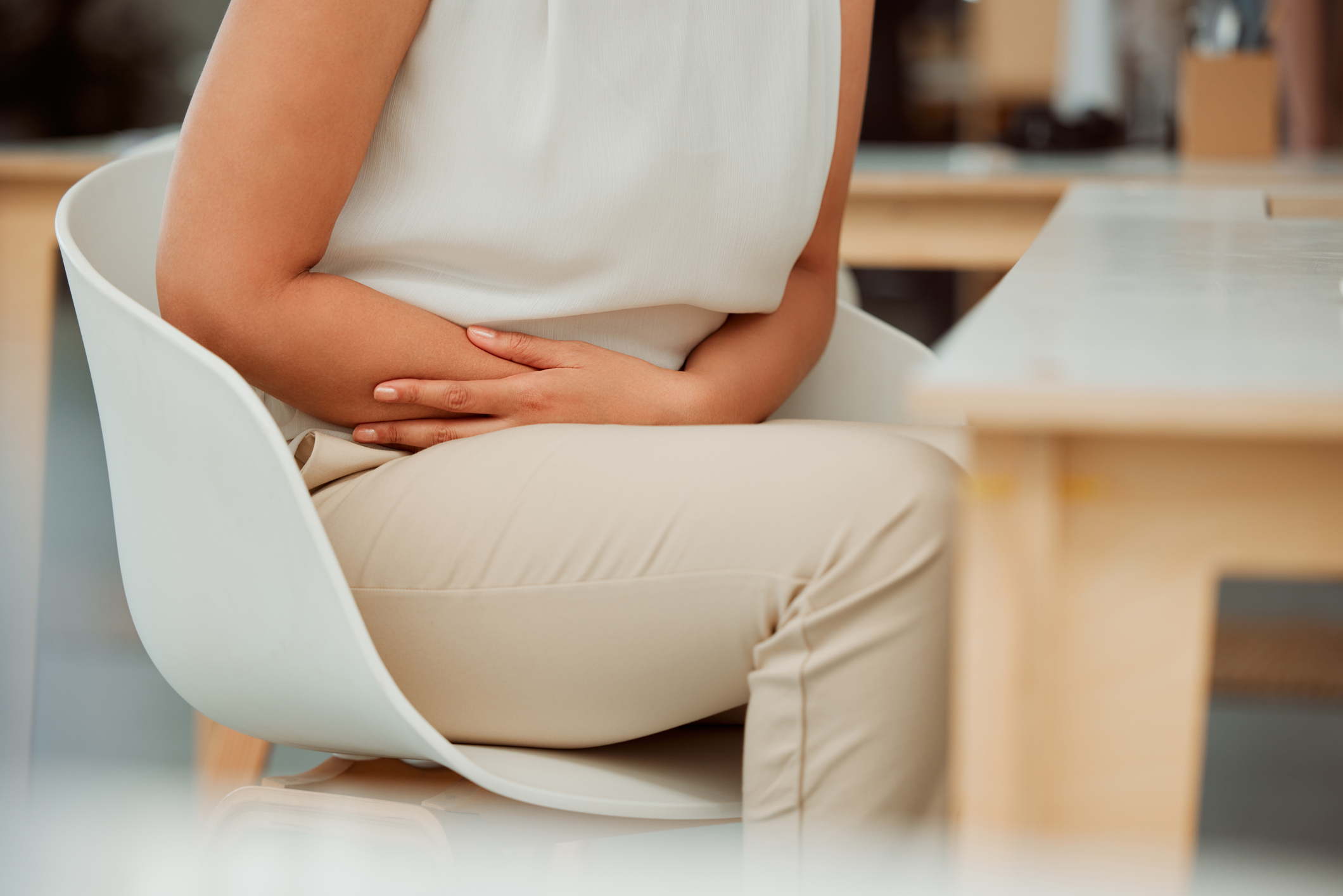 Woman experiencing abdominal discomfort from IBS while sitting at work.