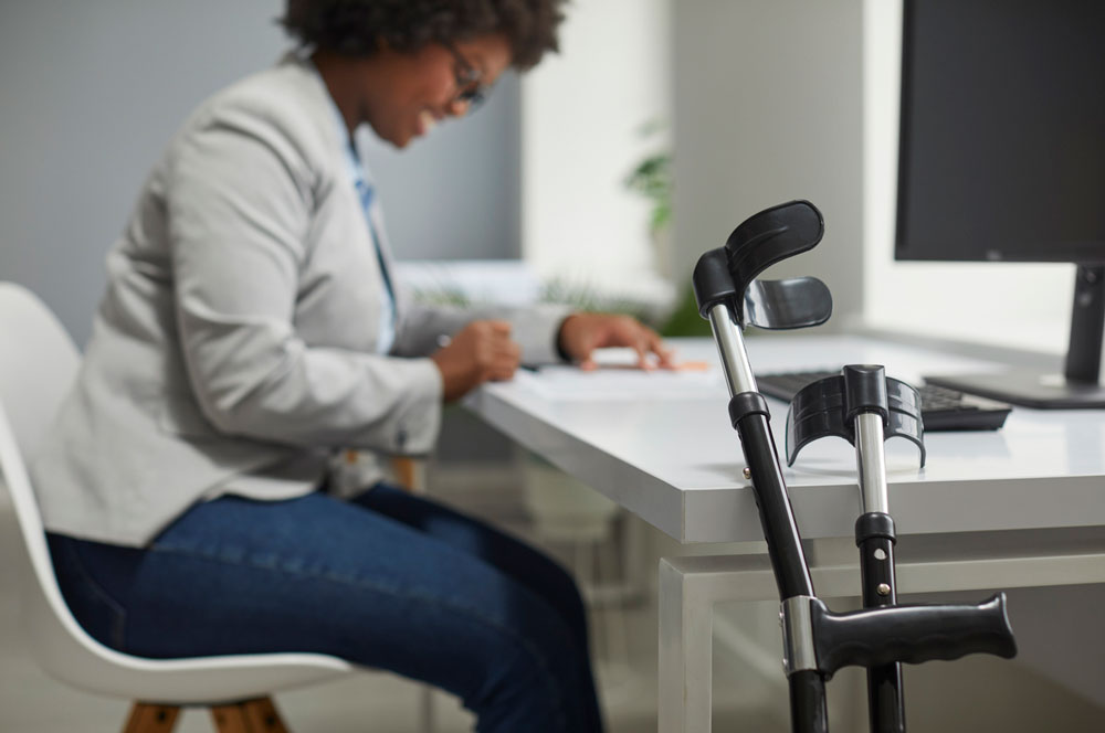 Crutches by office desk with happy disabled female employee working on computer